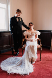Groom smiling at bride seated in a chair