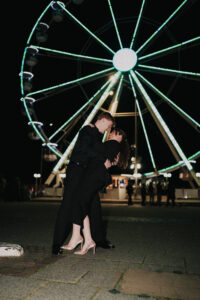 Portrait of bride and groom embracing each other in front of a ferris wheel in South Wales