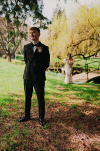 Groom smiling as bride stands behind, first look