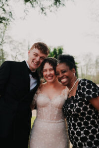 Bride and groom posing with wedding guest for group photo, candid moment