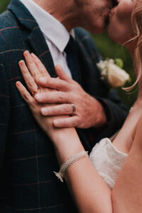 Bride and groom showing wedding bands while kissing during portrait session