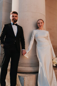 Formal portrait of bride and groom looking at the camera while holding hands