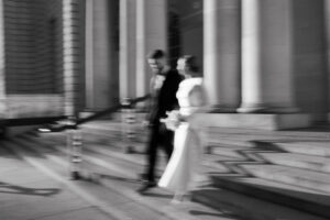 Blurry, black-and-white landscape of the bride and groom running down the stairs at Cardiff Museum