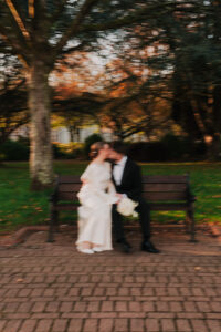 Wide portrait of bride and groom kissing on a park bench with motion blur