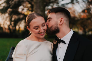 Groom kissing bride's cheek at golden hour