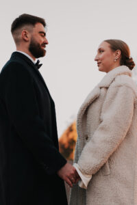 Close up of bride and groom holding hands in formal coats looking at each other