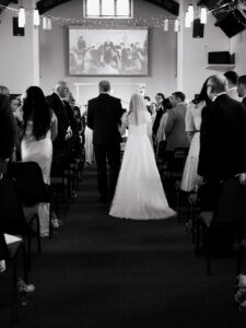 Black-and-white portrait of the bride and father of the groom walking down the aisle