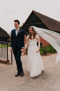 Bride's veil flying in the wind while holding the grooms hand, candid moment
